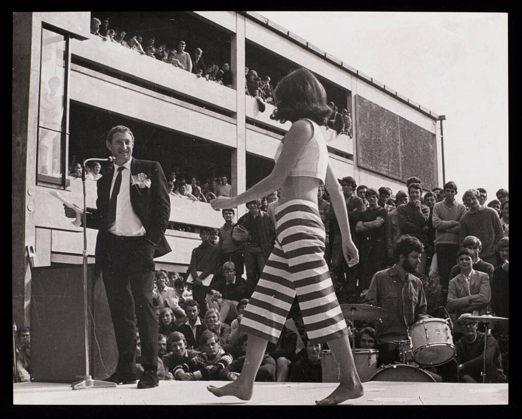 <p><a href="https://www.aucklandartgallery.com/explore-art-and-ideas/archives/19613/item/35954"><em>Maggy&nbsp;</em><em>Fashion Parade with Barry Crump, Auckland University</em></a>, black and white photographic print</p>