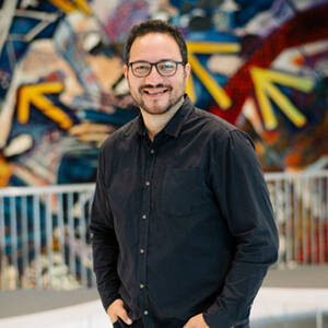 Caleb Matafeo smiles in front of a colourful mural in the Aotea Centre foyer.