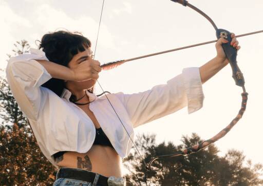 Erny Belle holding a bow and arrow aiming it to the sky, giving Katniss Everdeen imagery vibes