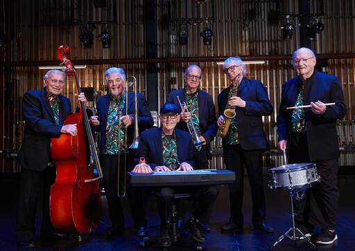 Society Jazzmen smiling with their instruments, dressed in navy blue jackets, colourful button up shirts, posing backstage.